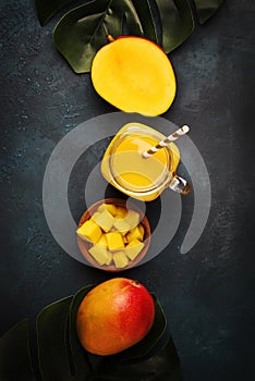 Freshly squeezed fresh mango juice in large glass jar with fresh fruit on dark blue background, place for text, top view
