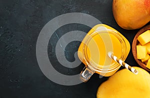 Freshly squeezed fresh mango juice in large glass jar with fresh fruit on dark blue background, place for text, top view