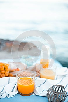 Freshly squeezed orange juice in a glass glass, ripe grapes and cheese on a blanket. Picnic by the sea. Healthy food and nutrition