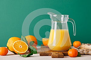 Freshly squeezed orange juice in a glass pitcher and fresh fruits with leaves, healthy drink, vitamin c concept, front view, copy