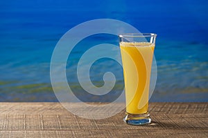 Freshly squeezed orange juice in glass on wooden table with sea water background on sunny summer day in tropical beach cafe, close