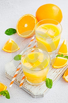 Freshly squeezed orange juice with ice in a glass with a straw on a wooden board on a light background with fresh oranges.