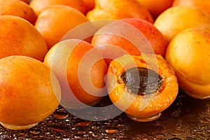 Freshly washed, ripe half sliced and whole apricots on a black cutting board with water drops and reflections