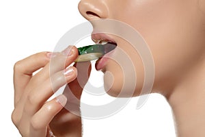 Freshness. Close up of beautiful young woman biting cucumber`s slice over white background. Cosmetics and makeup