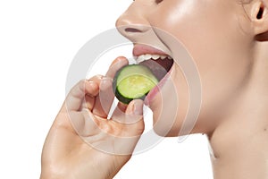 Freshness. Close up of beautiful young woman biting cucumber`s slice over white background. Cosmetics and makeup