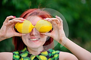 Freshness, healthy lifestyle and vitamins concept: smiling woman with red hair hiding her eyes behind two bright yellow lemons
