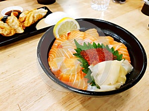 Freshness salmon sliced, salmon roe on green leaf and ginger top on rice and wooden table with blurred deep fried gyoza background