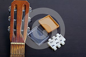 The fretboard of the acoustic guitar and the tuning fork to adjust it. On a dark background.