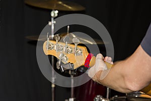 Fretboard of a five string bass guitar with a musician`s hand on the background of a drum kit in the Studio