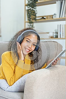 frican American sitting on a sofa using tablet and wearing headphones to relax