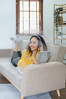 frican American sitting on a sofa using tablet and wearing headphones to relax