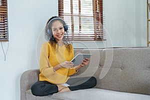 frican American sitting on a sofa using tablet and wearing headphones to relax