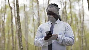 Frican man with shirt and tie using smartphone in he forest