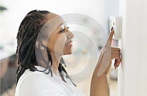 A frican woman lady adjusting the climate control panel on the wall wall thermostat