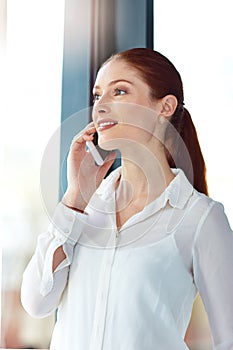 Friday on my mind. a thoughtful young businesswoman talking on the phone while looking out of her office window.