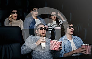 Friday night fun. Bewildered people in 3D glasses watching scary movie in cinema