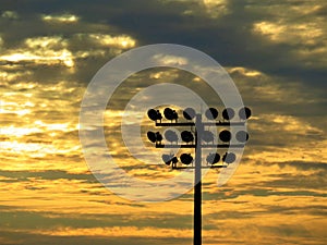 Friday night lights during the time of COVID: Playing field floodlights against clouds at sunset