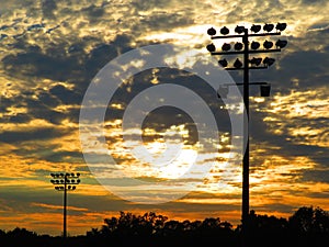 Friday night lights during the time of COVID: Playing field floodlights against clouds and trees at sunset #2