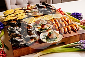 Fried and baked mussels in shells and baked scallops in shell with bacon and sliced lemon on wooden cutting board with card and