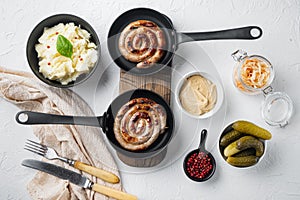 Fried Bavarian German NÃ¼rnberger sausages with sauerkraut  mashed potatoes in cast iron frying pan  on white background  top view