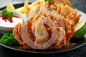 Fried Bloomin Onion with Chilli sauce and lime on black plate