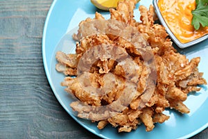Fried blooming onion with dipping sauce served on blue wooden table, top view