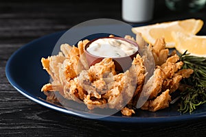 Fried blooming onion with dipping sauce served on dark wooden table, closeup