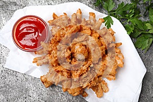 Fried blooming onion with dipping sauce served on grey table, flat lay