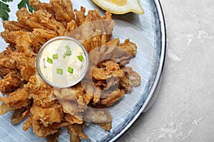 Fried blooming onion with dipping sauce served on light marble table, top view