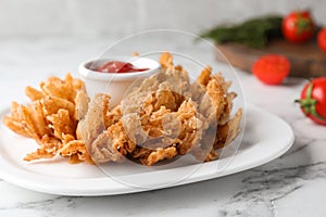 Fried blooming onion with dipping sauce served on white marble table, closeup