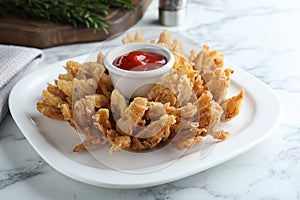 Fried blooming onion with dipping sauce served on white marble table, closeup