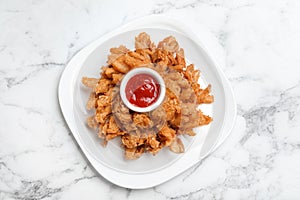 Fried blooming onion with dipping sauce served on white marble table, top view