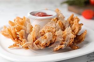 Fried blooming onion with dipping sauce served on white table, closeup