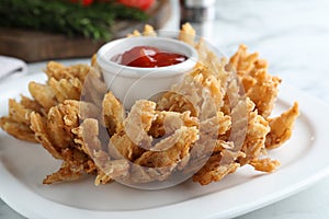 Fried blooming onion with dipping sauce served on white table, closeup