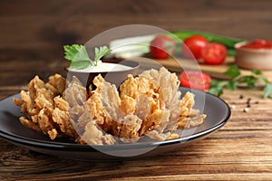 Fried blooming onion with dipping sauce served on wooden table, closeup