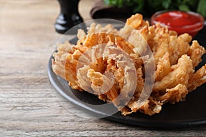 Fried blooming onion with dipping sauce served on wooden table, closeup