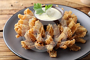 Fried blooming onion with dipping sauce served on wooden table, closeup