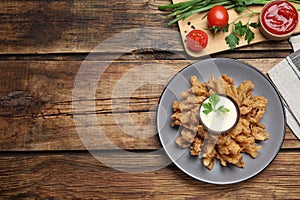 Fried blooming onion with dipping sauce served on wooden table, flat lay. Space for text