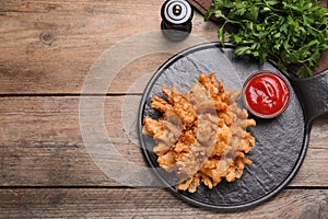 Fried blooming onion with dipping sauce served on wooden table, flat lay. Space for text