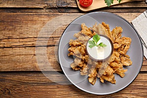 Fried blooming onion with dipping sauce served on wooden table, flat lay. Space for text