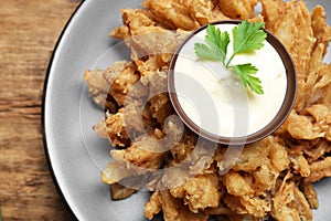 Fried blooming onion with dipping sauce served on wooden table, top view