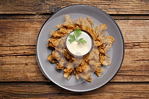 Fried blooming onion with dipping sauce served on wooden table, top view