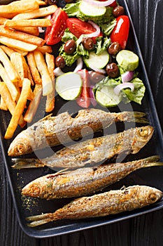 Fried boops boops fish with fresh vegetable salad and french fries close-up on a plate. Vertical top view photo