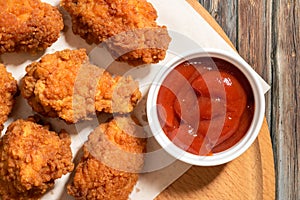 Fried breaded chicken strips with red sauce on a wooden tray.