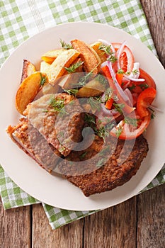 Fried Breaded rump steak with potato and vegetables close-up. vertical top view