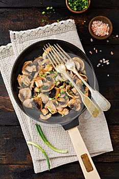 Fried Champignon mushrooms in a cast-iron old pan on an old dark wooden rustic background for frying. Top view