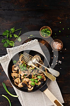 Fried Champignon mushrooms in a cast-iron old pan on an old dark wooden rustic background for frying. Top view