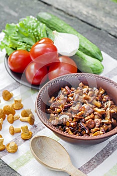 Fried chanterelles with onion in rustic bowl and plate with fresh vegetables for salad on background