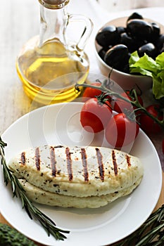 Fried cheese halumi on white plate, olive oil bottle, black olives, tomatoes, healthy food