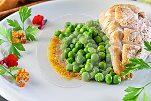 Fried chicken breast and broiled green peas on the decorated white dish closeup